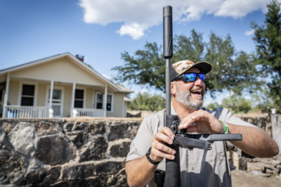 Hunter smiling outdoors while holding a rifle equipped with the Silencer Central Banish 30 Gold V2 suppressor.