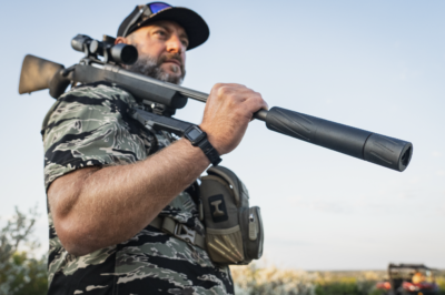 Hunter carrying a rifle equipped with the Silencer Central Banish 30 Gold V2 suppressor outdoors.