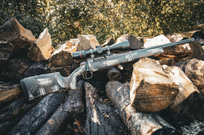 Weatherby Model 307 Alpine CT rifle with Burris optic resting on a stacked firewood pile in natural sunlight.